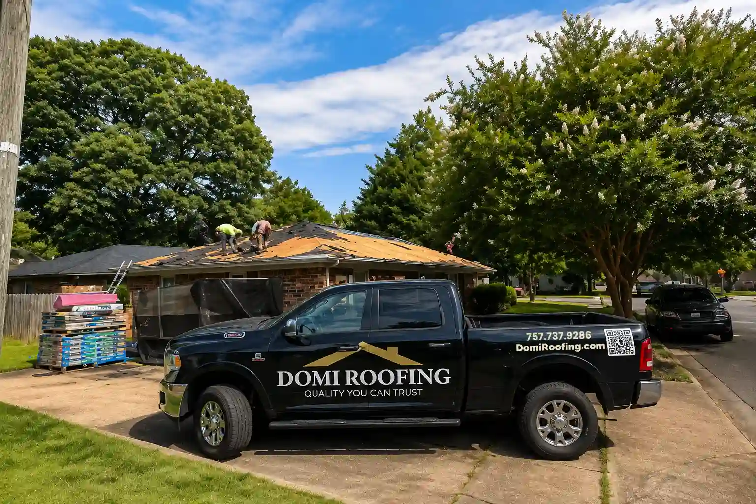 DOMI Roofing truck parked in front of a home during a roof replacement project, with roofing contractors removing old shingles and preparing the roof for new installation in Virginia Beach, VA.